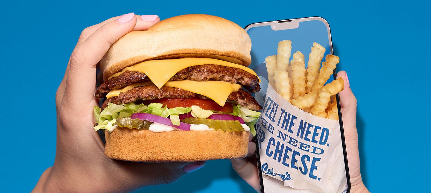 Hand holding burger and phone with fries