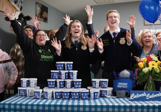 a group of people celebrate behind a table full of Culver's fresh frozen custard pints