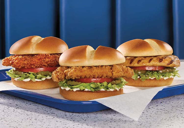 three chicken sandwiches of different styles on a tray on a table of a blue booth