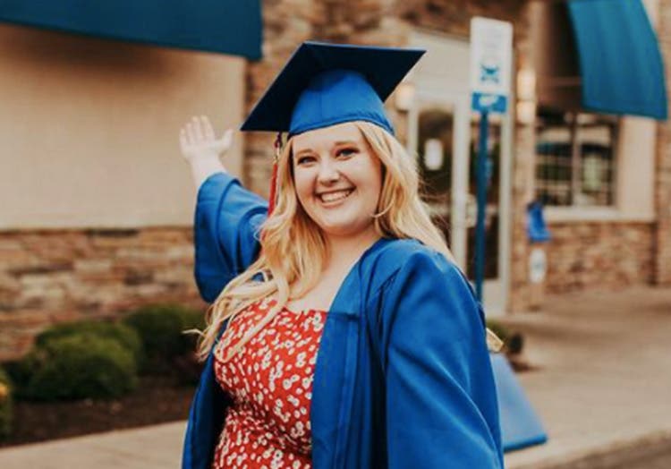 A young woman in her blue graduation cap and gown smiling in front of a Culver's.